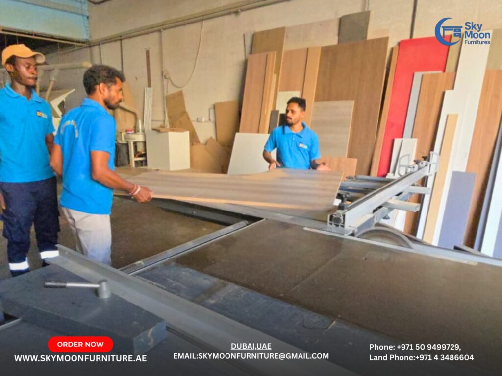 Three men in blue shirts collaborate on crafting a large wooden piece for custom office furniture manufacturing.