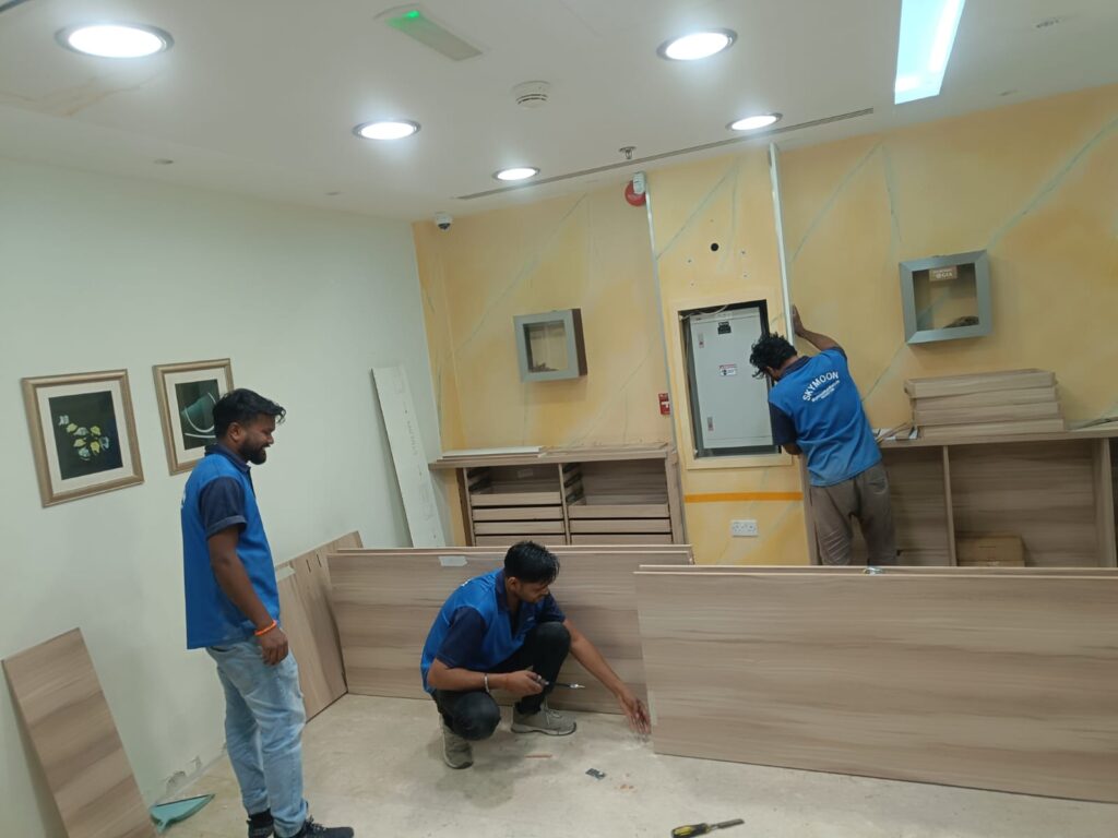 Men in blue shirts assembling a wooden cabinet, highlighting bespoke office furniture delivery in the UAE.